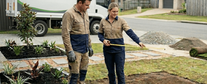Two landscapers measuring a residential front yard for a new project.